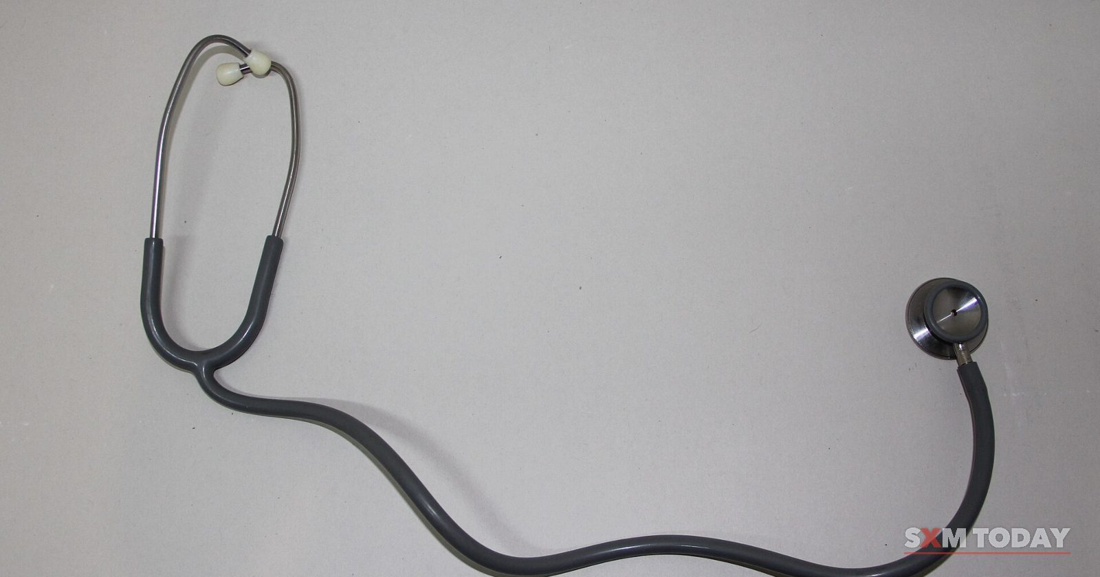 A black stethoscope laid out on a plain light grey surface.
