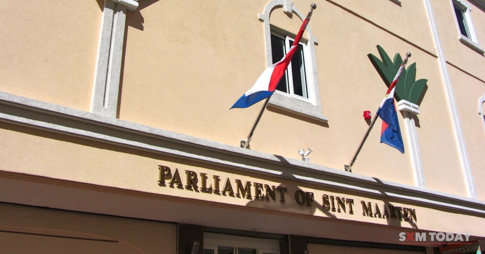 The Parliament of Sint Maarten building in Philipsburg, its name in raised letters beneath the Dutch and Sint Maarten flags.