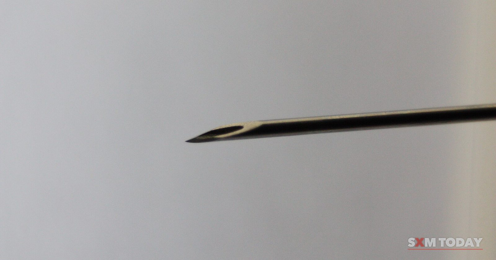 Close-up of the bevelled tip of a hypodermic needle against a plain grey background.