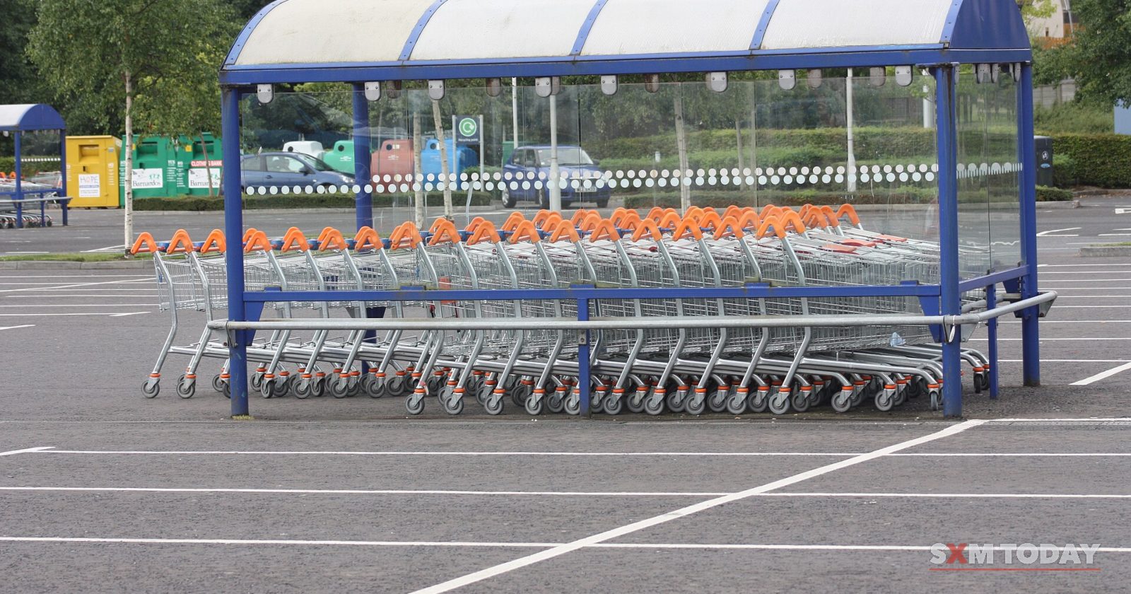 Rows of shopping trolleys parked under a blue shelter in an empty car park.
