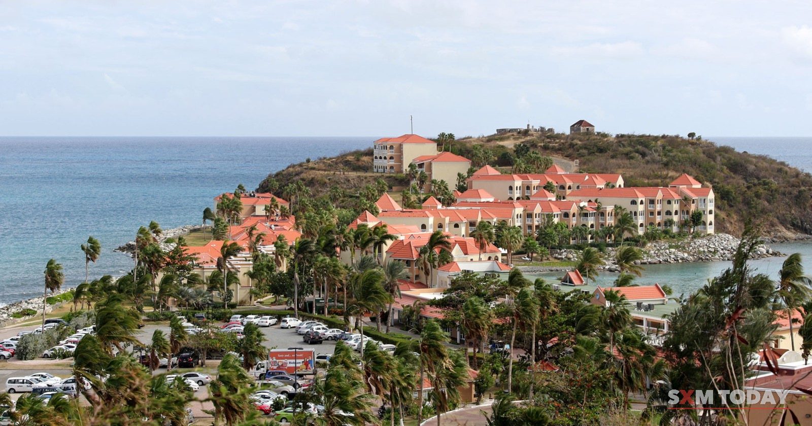 The Fort Amsterdam headland at Little Bay, with red-roofed buildings among palm trees.