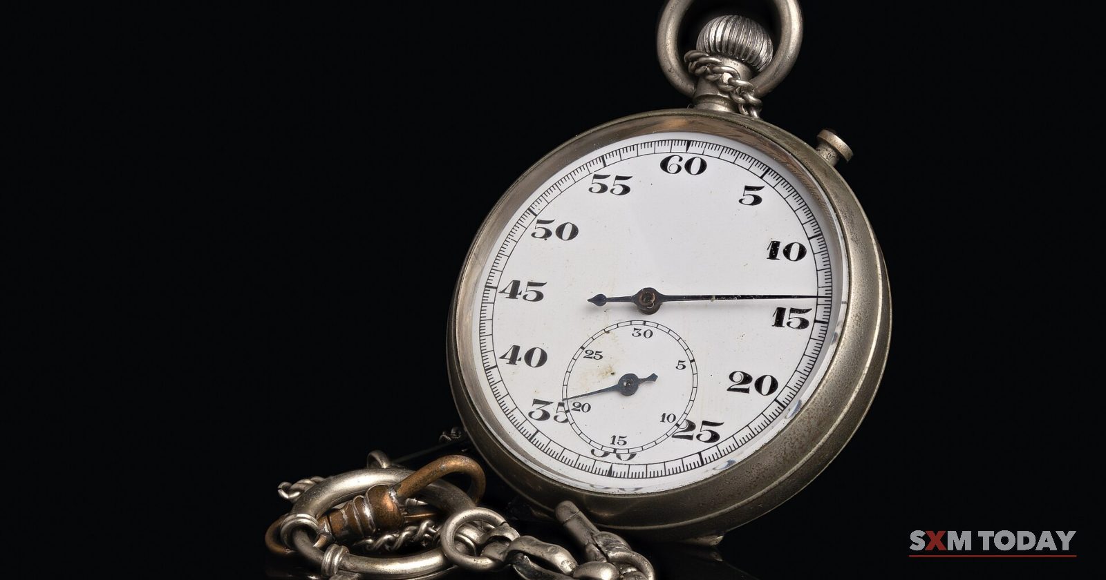 A silver stopwatch with a white dial and its chain, lit against a black background.