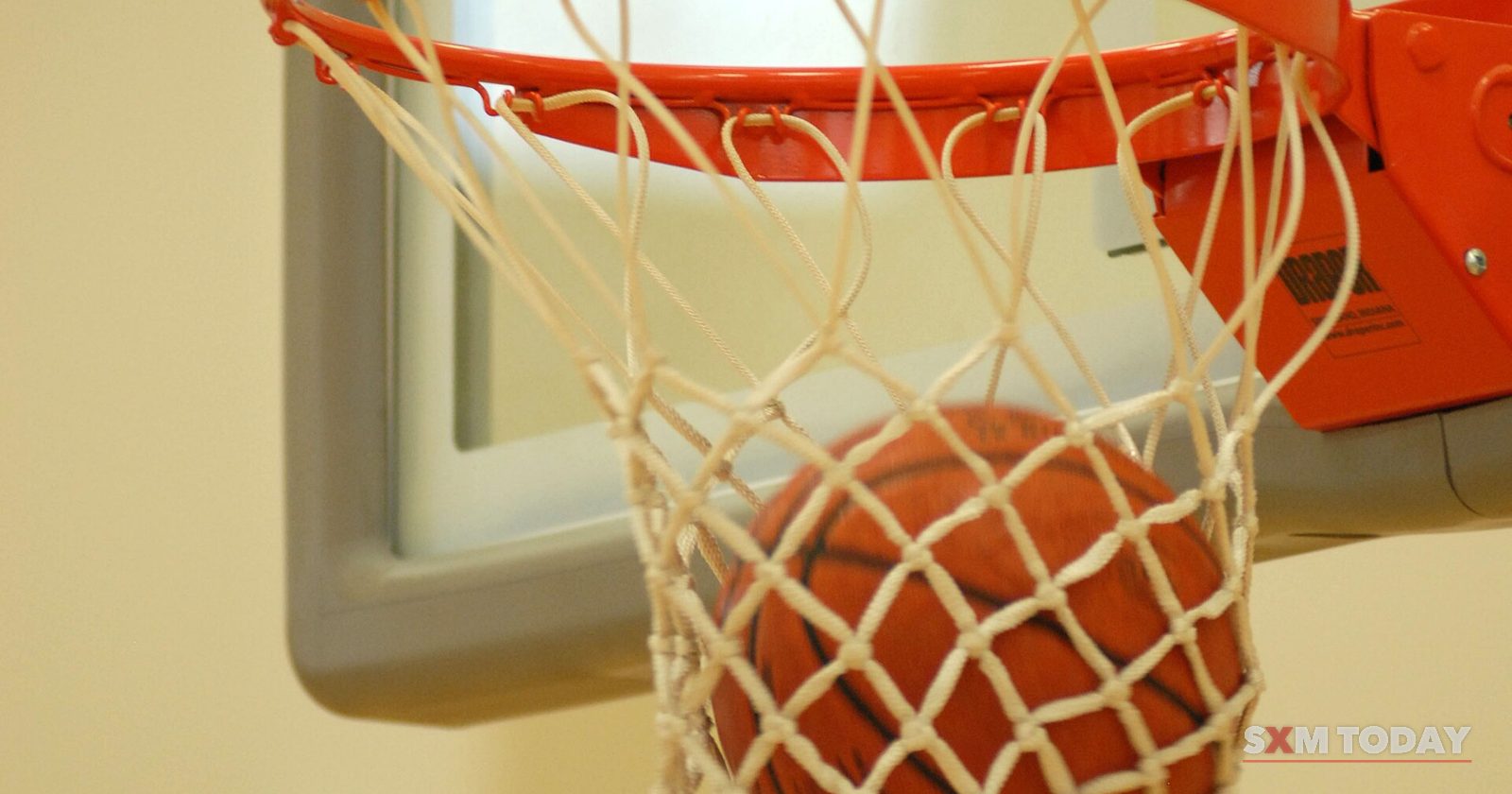 A basketball dropping through the net of an indoor hoop.