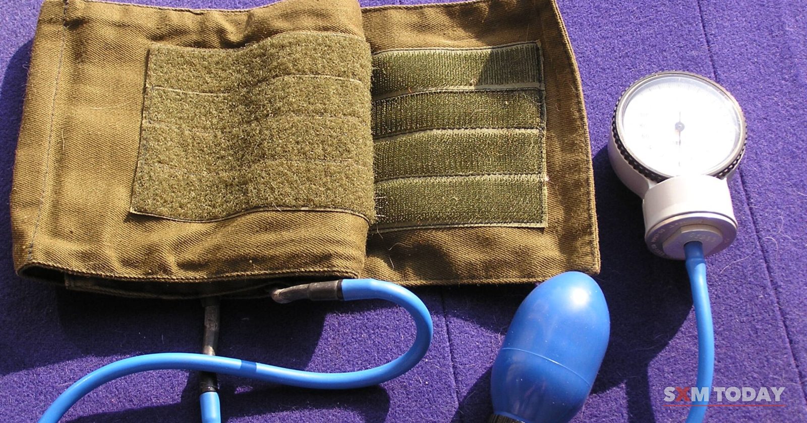 A manual blood pressure cuff with a dial gauge and blue rubber bulb laid out on a purple cloth.