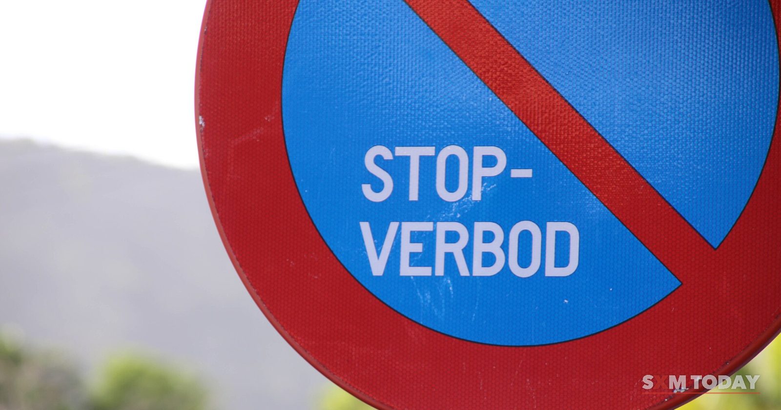 A round blue and red road sign reading Stop-verbod against a blurred green background.