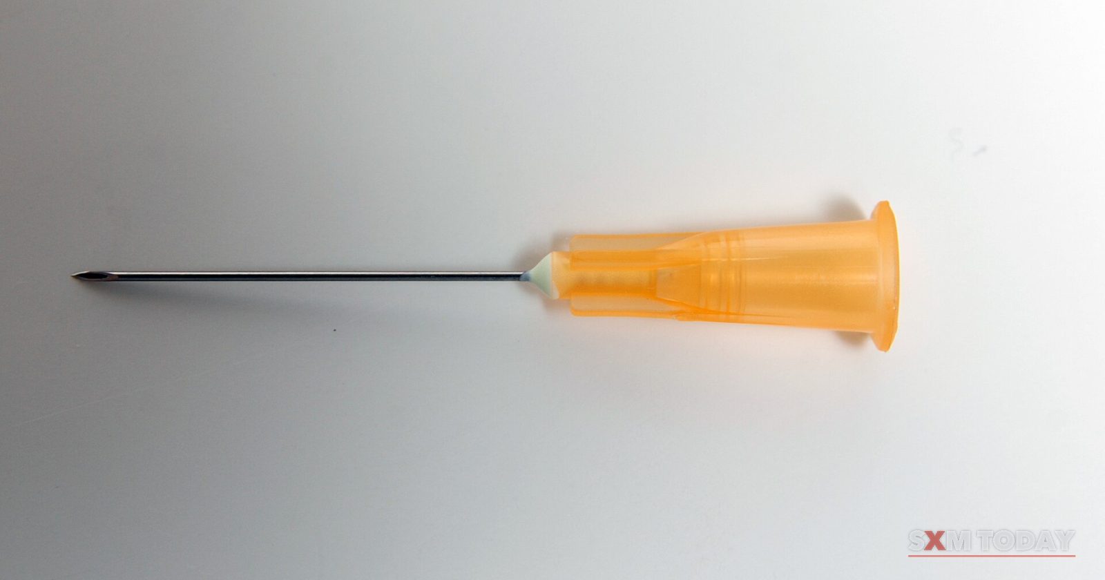 A single needle with an orange plastic hub lying on a plain white surface.