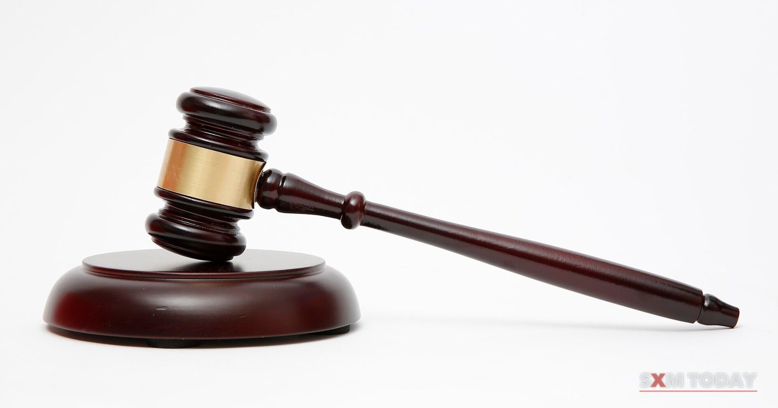 A dark wooden gavel with a brass band resting on its round sound block against a white background.