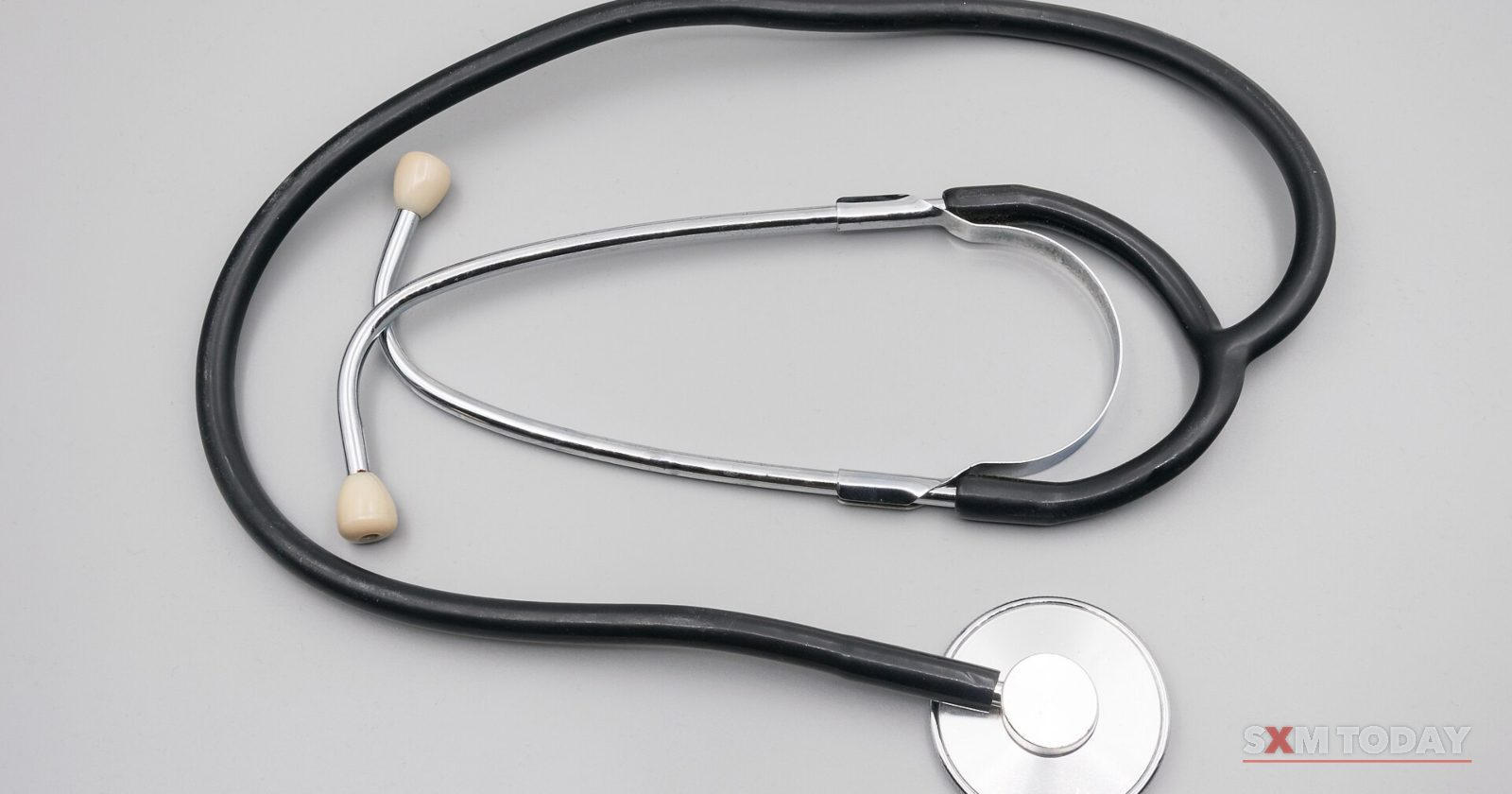 A black stethoscope lying coiled on a plain grey surface.