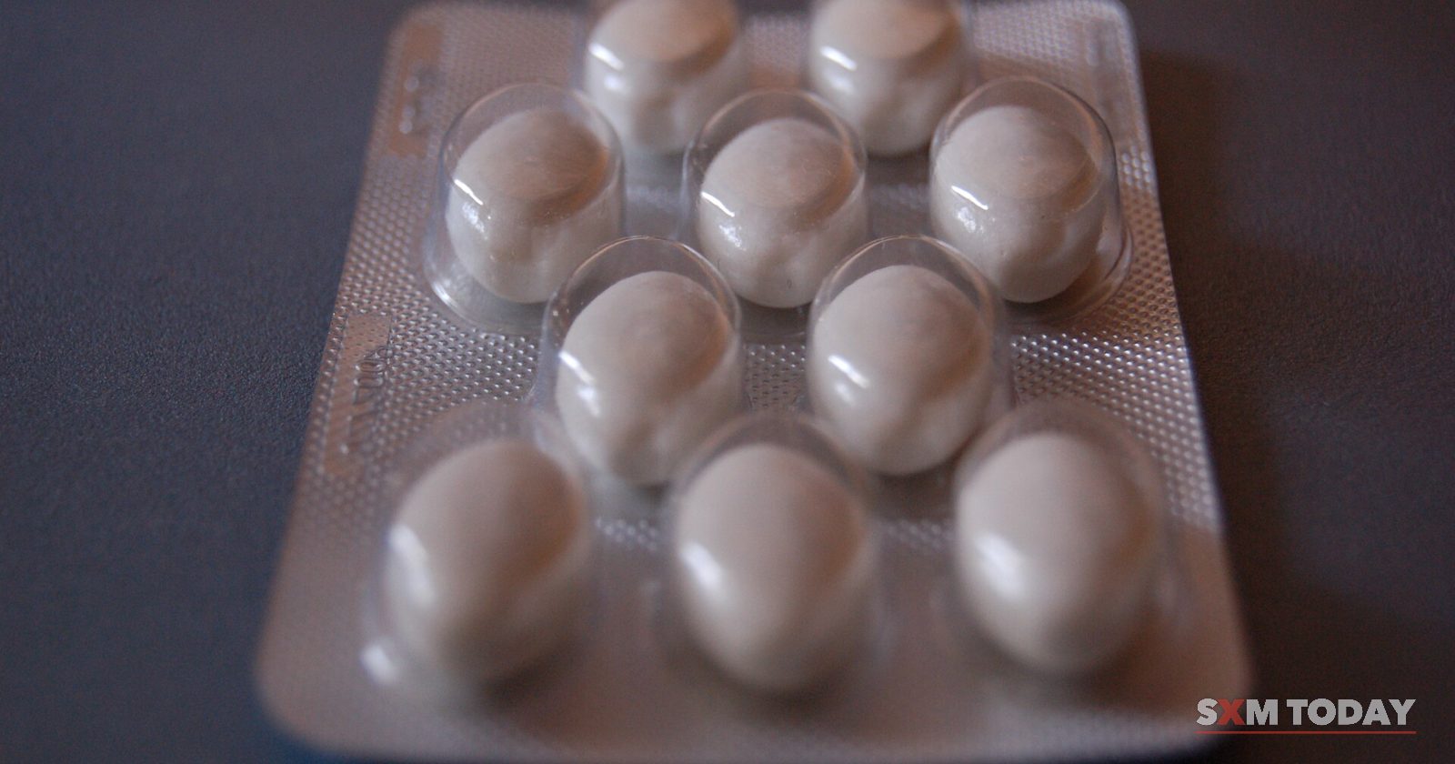 A blister pack of round white tablets on a dark surface.